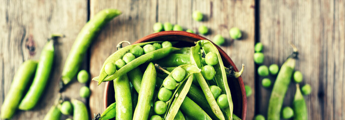 Wall Mural - Green peas and pods in a clay bowl on a wooden table, top view, rural style