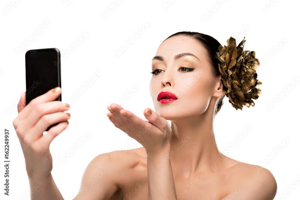 Beautiful naked young woman blowing a kiss while taking selfie on smartphone Stock Photo | Adobe