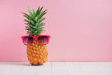 Funny pineapple in a sunglasses on table over pink background