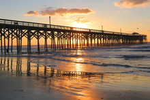 Sunrise At A South Carolina Atlantic Coast, Myrtle Beach Area, USA. Landscape With The Reflection Of The Sun In Shallow Water On The Foreground And A Wooden Pier On The Background.Vacation Background.