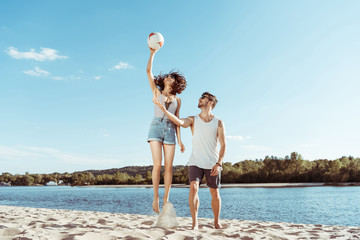 happy active man and woman playing volleyball on beach together