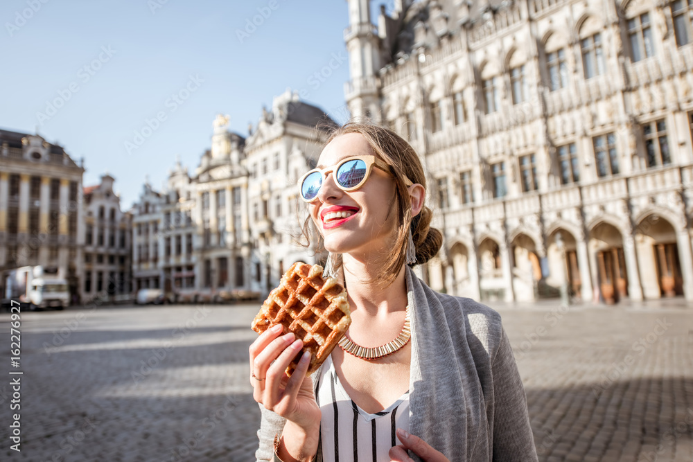 Obraz na płótnie Young woman walking with waffle a traditional belgian pastry food in the center of Brussels city during the morning w salonie