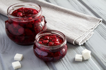 Raspberry jam in two glass jars on the grey wooden background