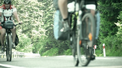 Two unidentified male bicycle tourists climbing up the mountain asphalt road. Hot summer day heat haze