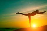 Fototapeta Pokój dzieciecy - Yoga and healthy lifestyle. Silhouette of fitness woman doing exercises on the sea beach during amazing sunset.