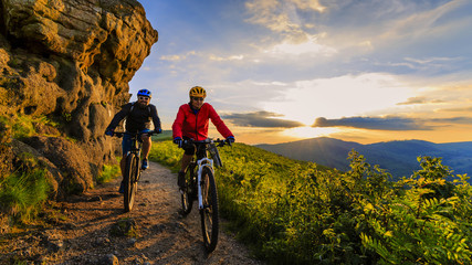 mountain biking women and man riding on bikes at sunset mountains forest landscape. couple cycling m