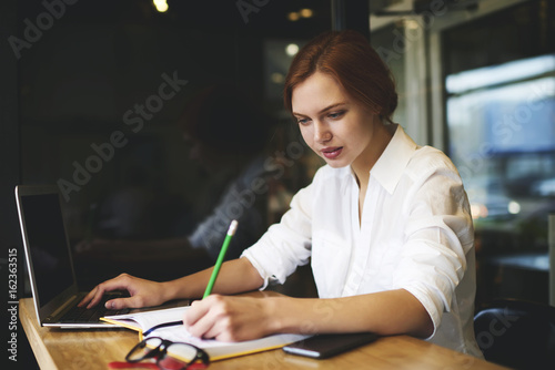 Fotografie, Obraz Concentrated talented female author writing essay using laptop computer for brow