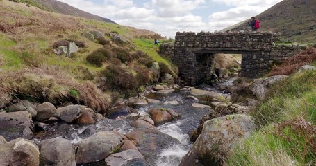 Wall Mural - A hiker and their dog crossing an old stone bridge over Grainsgill Beck in the Caldbeck Fells in the English Lake District, UK.