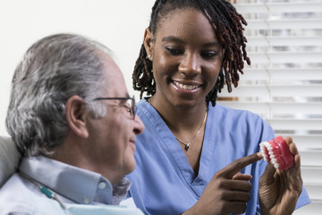 Dental hygienist showing senior male about teeth cleaning