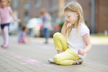 cute little girl drawing with colorful chalks on a sidewalk. summer activity for small kids.