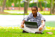 Young black man sitting down on green grass and working in his computer in the city of Quito Ecuador