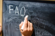 Child hand drawing FAQs - Frequently Asked Questions text on the blackboard. Education thoughts hot ideas