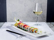 Rainbow sushi roll with salmon and avocado, complete with a glass of white wine