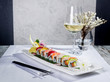 Rainbow sushi roll with salmon and avocado, complete with a glass of white wine and a tempura decoration