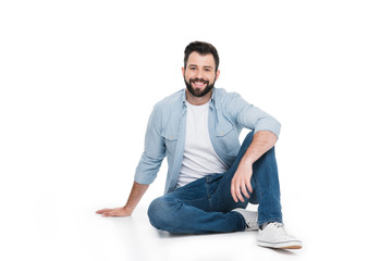 handsome young bearded man sitting and smiling at camera isolated on white