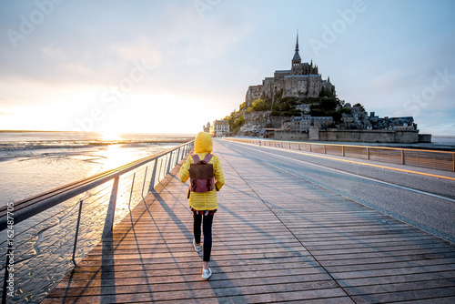 Young female traveler in yellow raincoat on the road to famous saint Michel isla плакат