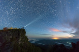 Fototapeta Zachód słońca - Star trail over the mountain with the man light up the sky before sunsire, Nan Province, Thailand
