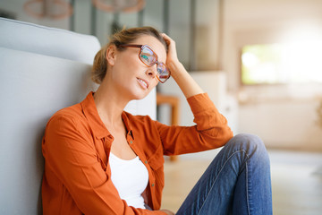 Wall Mural - Cheerful girl with trendy eyeglasses sitting on floor at home