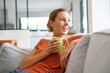 © goodluz - Cheerful woman relaxing in sofa and drinking tea