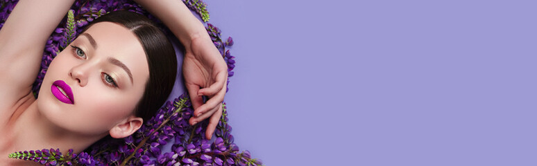 Wall Mural - Beautiful young girl is surrounded by purple flowers. Blue flowers.
Lilac lipstick. Cosmetic products for skin care.