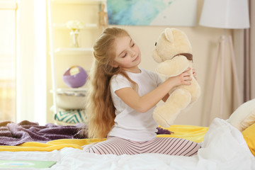 Wall Mural - Small girl playing with teddy bear on bed in light room