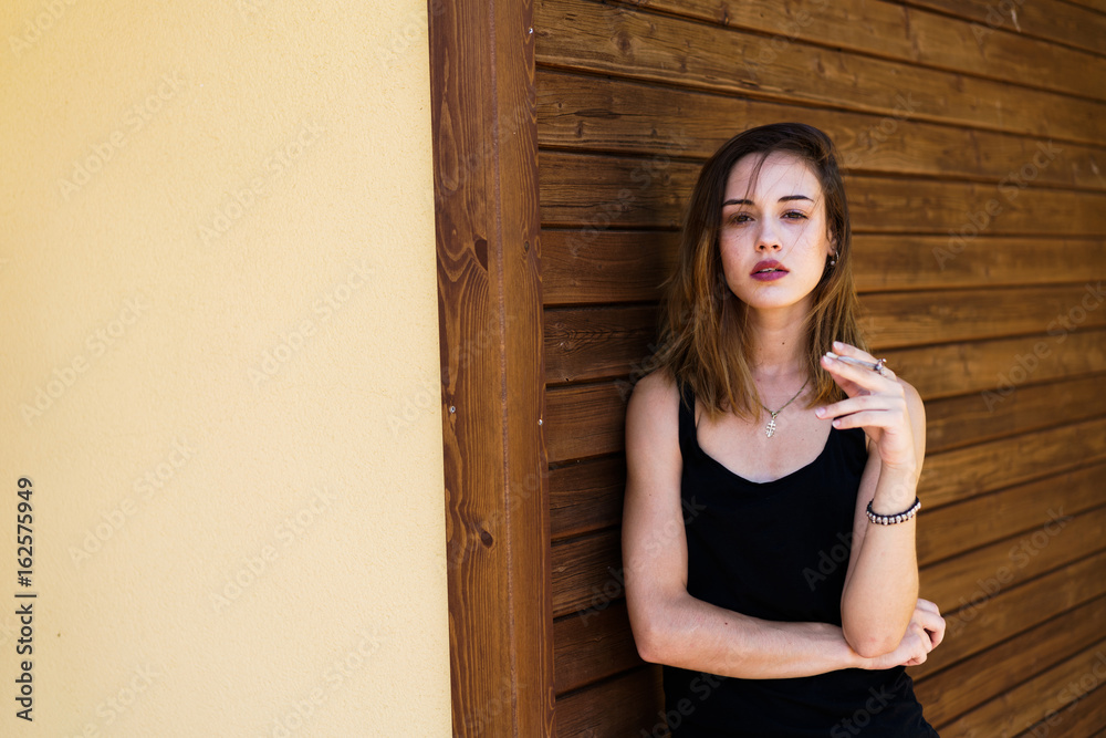 Young woman smoking cigarette while standing outside of house Stock Photo