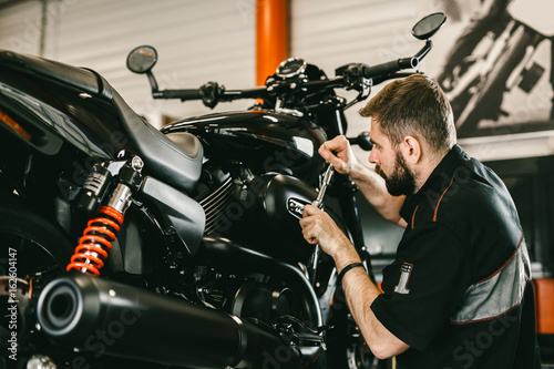 Zdjęcie XXL Profesjonalny mechanik naprawy śrubokręt i motocykl. Przystojny młodego człowieka naprawiania motocykl w remontowym sklepie.