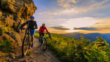 Mountain Biking Women And Man Riding On Bikes At Sunset Mountains Forest Landscape. Couple Cycling MTB Enduro Flow Trail Track. Outdoor Sport Activity.