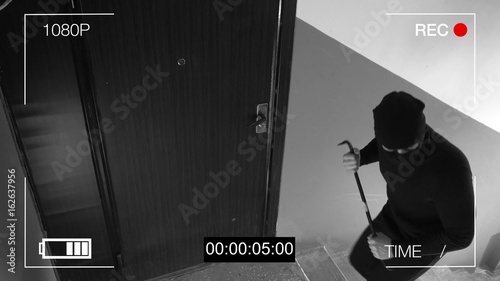 Fotografía See CCTV as a burglar breaking in through the door with a crowbar