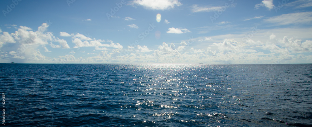 A panoramic scene of blue sky and the ocean with sunbeam shine above - obrazy, fototapety, plakaty 