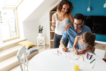 Father and mother teach daughter to draw.They sitting in living room and making fun.