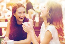 Smiling Young Women With Coffee Cups At Cafe