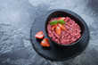 Black bowl with strawberry risotto on a stone slate tray, studio shot over grey stone background