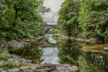 A View Down A River With A Bridge Spanning It And With Reflections In The Water. A Typical British Country Scene