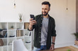 © LIGHTFIELD STUDIOS - Handsome smiling man using smartphone while standing in office