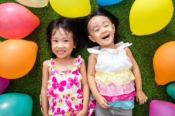 Wall Mural - Asian little Chinese girls lying on grass amongst colorful balloons