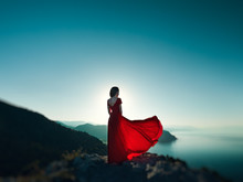 Young Beautiful Woman In Red Dress Looking To Mountains Sea