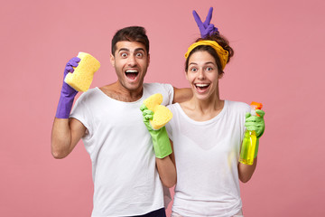 young male and female playing fools while standing against white pink wall resting after doing clean