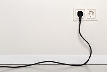 Black Power Cord Cable Plugged Into European Wall Outlet On White Plaster Wall