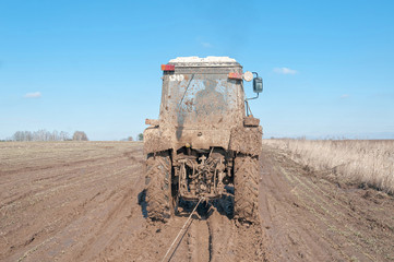 Wall Mural - Wheeled tractor tows in mud on dirt road in fallow field
