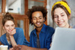 © wayhome.studio  - Portrait of three mixed race friends meeting together watching their photos with laptop having delightful expression. Two European females and African guy having concentrated look in screen of laptop