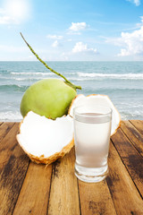 Wall Mural - Sliced coconut with coconut juice on wooden table with sea view background.