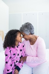 Wall Mural - Smiling granddaughter and grandmother sitting face to face on bed