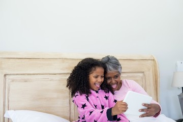 Wall Mural - Grandmother and granddaughter taking selfie on digital tablet in bed room