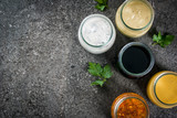 Set of organic healthy dietary dressings for salad: sauce vinaigrette, mustard, mayonnaise with spices or ranch, balsamic or soy, basil with yogurt. On a dark stone table. Top view copy space
