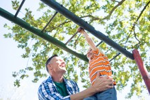 Father Holding Son Playing On Jungle Gym At Playground