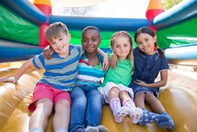 Portrait Of Friends With Arms Around Sitting On Bouncy Castle