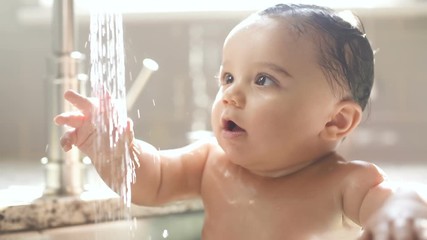 baby in awe of water stream from sink faucet. a stream of water pouring out of the faucet and baby l