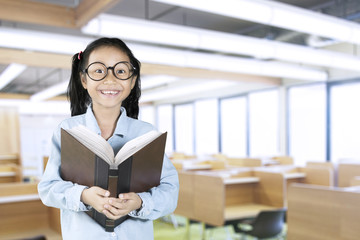 Wall Mural - Schoolgirl smiling at camera with book in classroom