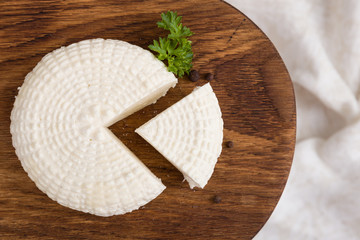 Top view on sliced round white homemade cheese  - traditional milk creamy dairy product on vintage wooden board. Rustic style.